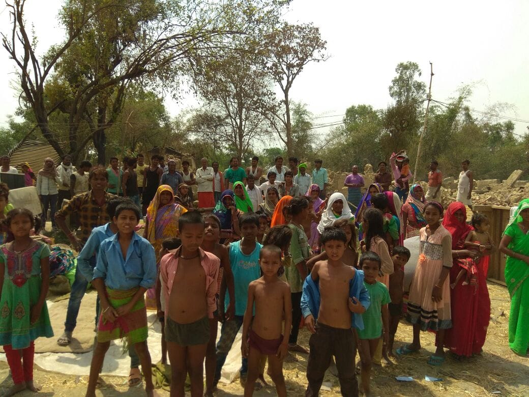 Pasi community members seek refuge on a field near the pond after their homes burnt down Sunday