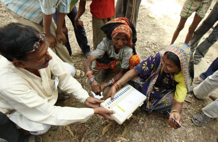 A polling official, left, instructs voters how to use the Electronic Voting Machines | Pankaj Nangia/Bloomberg News