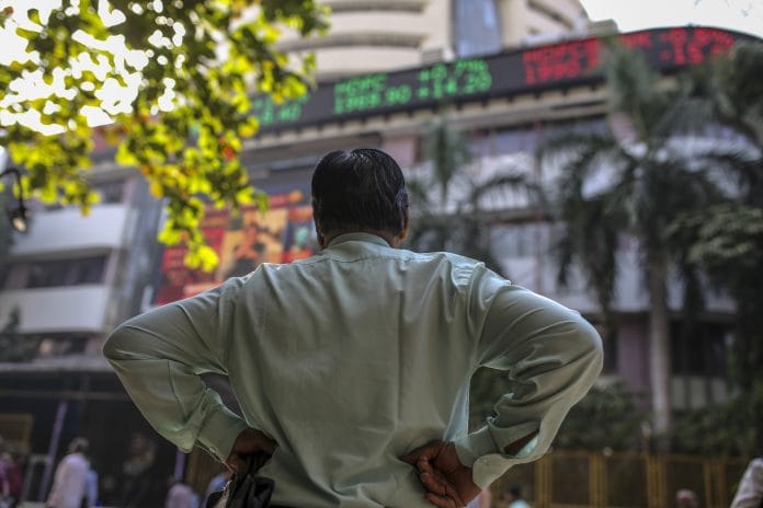 A man stands in front of an electronic ticker board showing stock information figures outside the Bombay Stock Exchange (BSE) in Mumbai