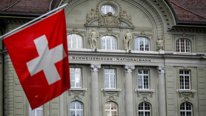 A Swiss national flag hangs in view of the Swiss National Bank (SNB) in Bern, Switzerland