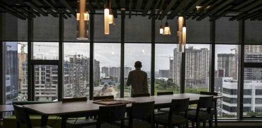 An employee standing at the window looks out over construction sites from the Amazon.com Inc. office campus in Hyderabad