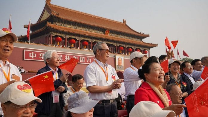 Attendees of the military parade sing a song and wave national flags before the parade begins in Tiananmen Square in Beijing, China | Andrea Verdelli | Getty Images