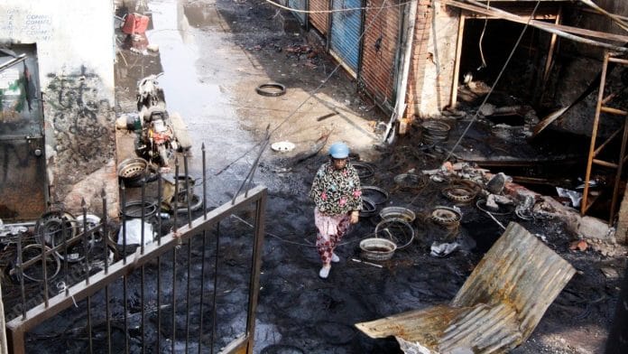 A woman walks past the burnt tyre market in Gokulpuri, Delhi | Praveen Jain | ThePrint