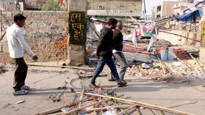 People walk by a sign reading 'hum ek hain' (we are one) in riot-hit Mustafabad in Northeast Delhi | Photo: Praveen Jain | ThePrint
