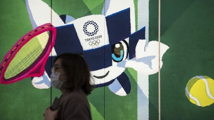 Woman wearing a mask crosses a Tokyo Olympics sign | Bloomberg