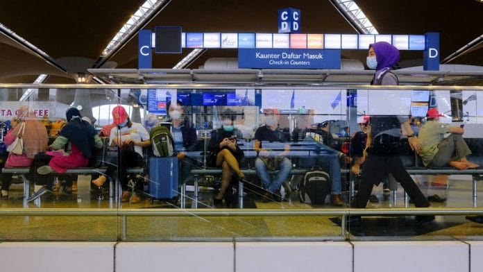 People wearing protective masks as she walk in front the Air Asia ticket counter at Kuala Lumpur International Airport (KLIA) in Sepang, Malaysia. | Photographer: Samsul Said | Bloomberg