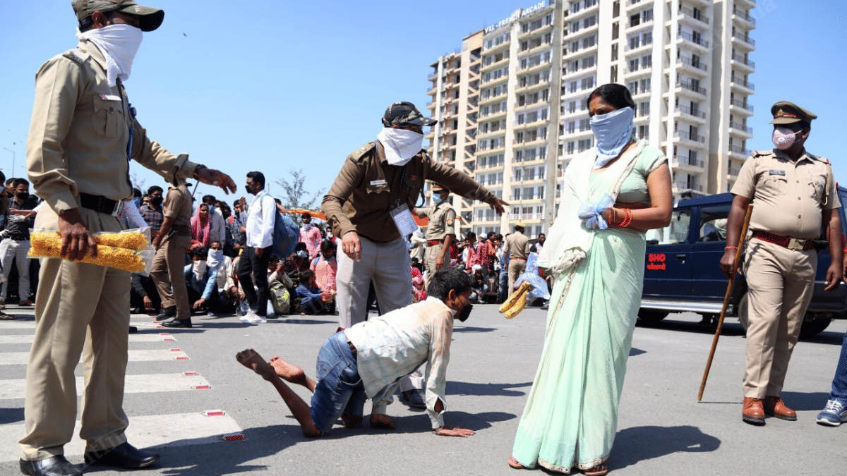 UP police guide a specially abled man to a bus. In the background, one can see long queues of workers waiting to board | Photo: Suraj Singh Bisht | ThePrint