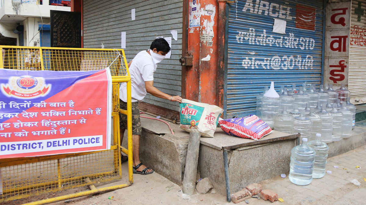 A resident picks up essential goods from the barricade at the end of a lane in Tughlaqabad Extension | Photo: Manisha Mondal | ThePrint