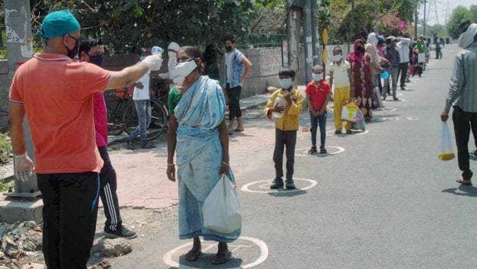 A health worker checks the temperature of a woman, during distribution of food among the needy, amid the nationwide lockdown to curb the spread of coronavirus, at Sec-33 in Noida. | PTI