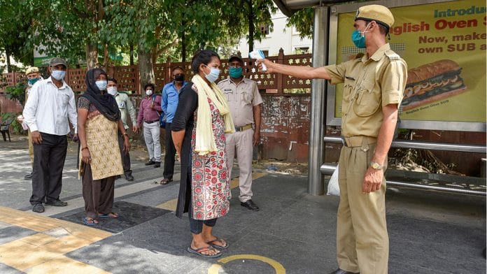 A Delhi homeguard conducts a thermal screening of passengers at a bus stop during the Covid-19 lockdown