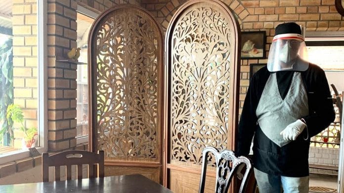 A waiter in a mask and visor stands next to wooden screens separating tables in Cafe Diem, Coonoor | Photo: Radhika Shastry