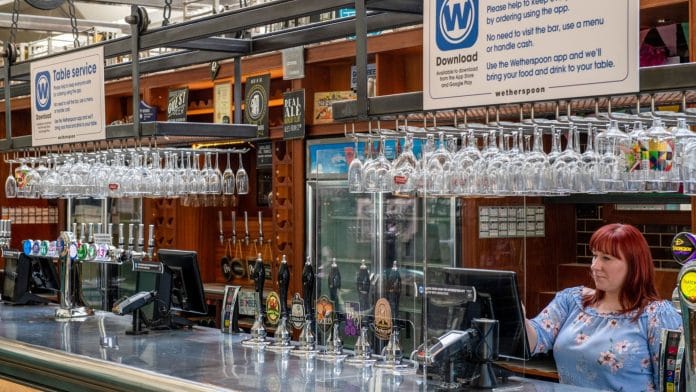 An employee checks a till behind a perspex screen at The Mossy Well pub in London | Photographer: Chris J. Ratcliffe | Bloomberg