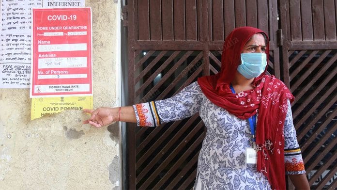 An ASHA worker, pastes a Covid-19 isolation poster outside a patient's house | Manisha Mondal | ThePrint