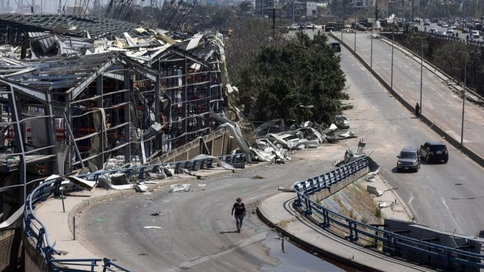 A pedestrian walks along a road past destroyed commercial warehouse buildings in Beirut, Lebano | Photographer: Hasan Shaaban | Bloomberg