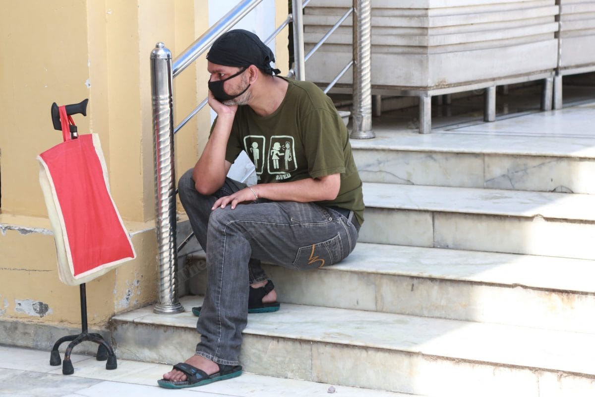 A physically handicapped man sits on the stairs while waiting for his turn | Photo: Manisha Mondal | ThePrint