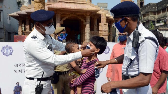 Kolkata Police personnel make a child wear a mask outside a Durga Puja pandal Tuesday | Photo: ANI