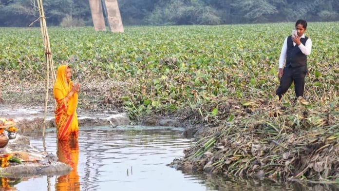 A woman performs puja while standing in a pond worshippers found near the Delhi-Noida border, on 20 November 2020 | Photo: Praveen Jain | ThePrint