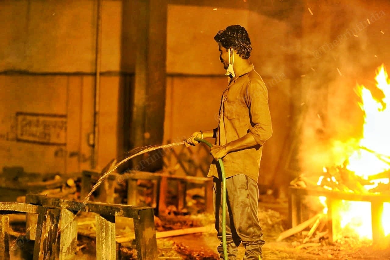 A crematorium workers puts water over the fire of cremation | Photo: Praveen Jain | ThePrint