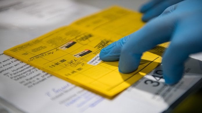 A doctor puts a sticker for the Pfizer/BioNTech vaccine against Covid-19 in a certificate of vaccination in Germany | Photo by Jens Schlueter/Getty Images via Bloomberg