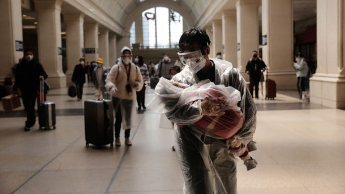 A man carrying a child, both wearing protective masks and raincoats, walk inside the Hankou railway station in Wuhan, China | Representational image | Bloomberg