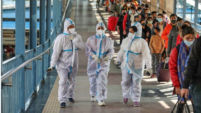 Health workers walk past the passengers waiting in a queue during Covid testing at Katra railway station in Jammu, on 6 December 2021 | PTI