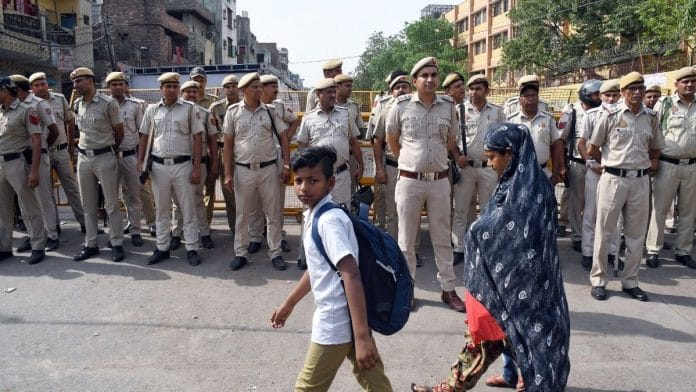 People walk past police personnel standing guard at a site after clashes broke out between two communities during procession on Hanuman Jayanti, at Jahangirpuri, in New Delhi on 19 April 2022 | Photo: ANI