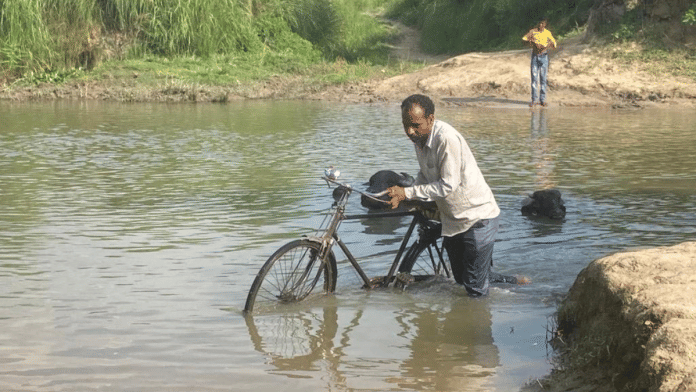 Villagers forced to wade through a channel flowing by the Usarhawa village of Sohagi Barwa Sanctuary area in Maharajganj district. The only wooden bridge that linked the village with the Maharajganj city collapsed last year during rainfall | Shikha Salaria