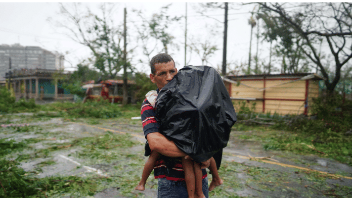 File Photo- A man carries his children next to debris caused by the Hurricane Ian after it passed in Pinar del Rio, Cuba, 27 September, 2022. Reuters/Alexandre Meneghini