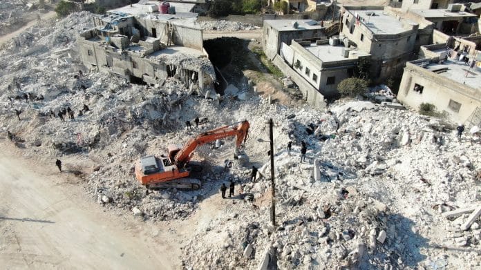 A machinery operates at the site of damaged buildings in the aftermath of an earthquake, in rebel-held town of Harem, Syria on 13 February 2023 | Photo: Reuters