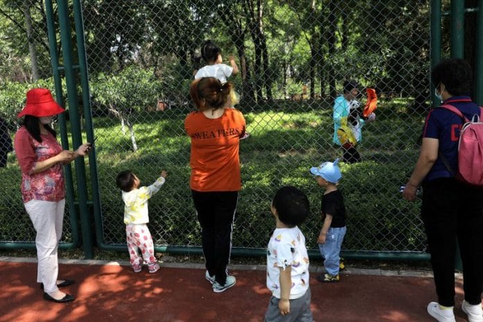 Children play next to adults at a park in Beijing, China | Reuters