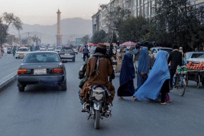 A group of women wearing burqas crosses the street as members of the Taliban drive past in Kabul, Afghanistan | Reuters file photo