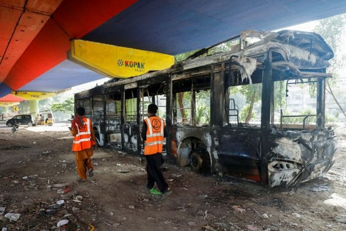 People walk past a public bus, which was set afire by supporters of Pakistan's former PM Imran Khan during a protest against his arrest, in Karachi, on 10 May 2023 | Reuters