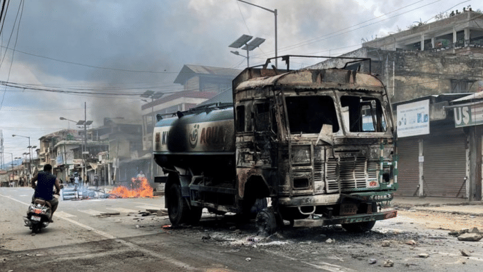 A scooterist rides past a damaged water tanker that was set afire during a protest by tribal groups in Churachandpur in Manipur, on 4 May 2023 | Reuters