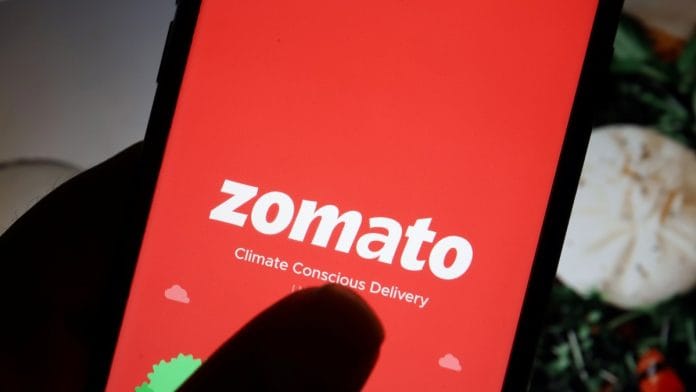 The logo of Indian food delivery company Zomato is seen on its app on a mobile phone displayed in front of its company website | Reuters
