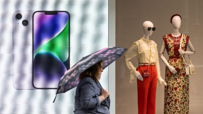 A woman with an umbrella walks past a display advertising Apple iPhone 14 during rainy weather in Moscow, Russia | Reuters