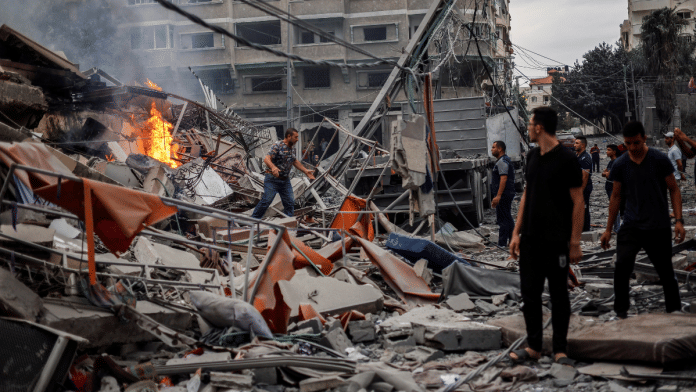 Palestinians watch a fire burn among the rubble of a damaged residential building, in the aftermath of Israeli strikes in Gaza City | Reuters