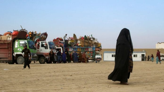 An Afghan national woman in a burqa walks past trucks loaded with belongings, as Afghan nationals in Pakistan head back to Afghanistan, at the Friendship Gate of Chaman Border Crossing along the Pakistan-Afghanistan Border in Balochistan Province, in Chaman, Pakistan on 8 November, 2023 | REUTERS/Naseer Ahmed