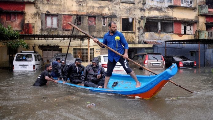 People move in a boat past partially submerged vehicles in a residential area following heavy rains ahead of Cyclone Michaung in Chennai, India | Reuters