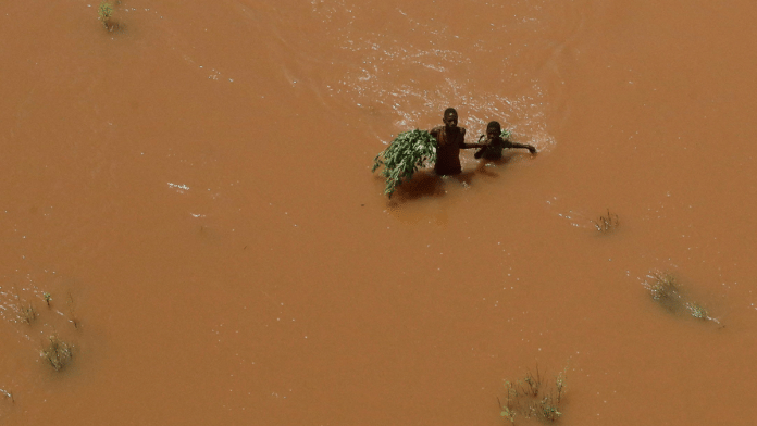People hold on to plants as they wade through flood waters after they were displaced following heavy rains in Kenya | Reuters/Thomas Mukoya/File Photo