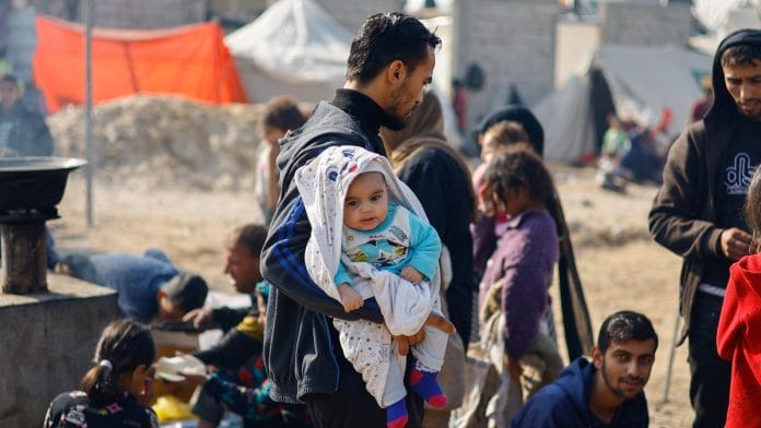 A man holds a baby as displaced Palestinians, who fled their homes due to Israeli strikes, shelter in a tent camp, amid the ongoing conflict between Israel and the Palestinian Islamist group Hamas, in Rafah, southern Gaza Strip, January 1, 2024 | Reuters