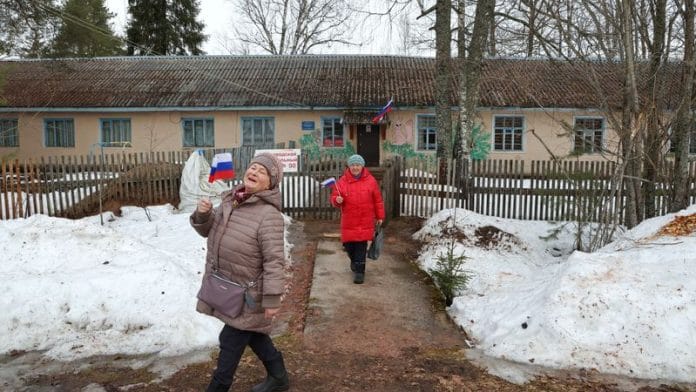 Women carry Russian flags as they leave a polling station during the presidential election in the village of Pasha in the Leningrad Region, Russia March 16, 2024. REUTERS/Anton Vaganov