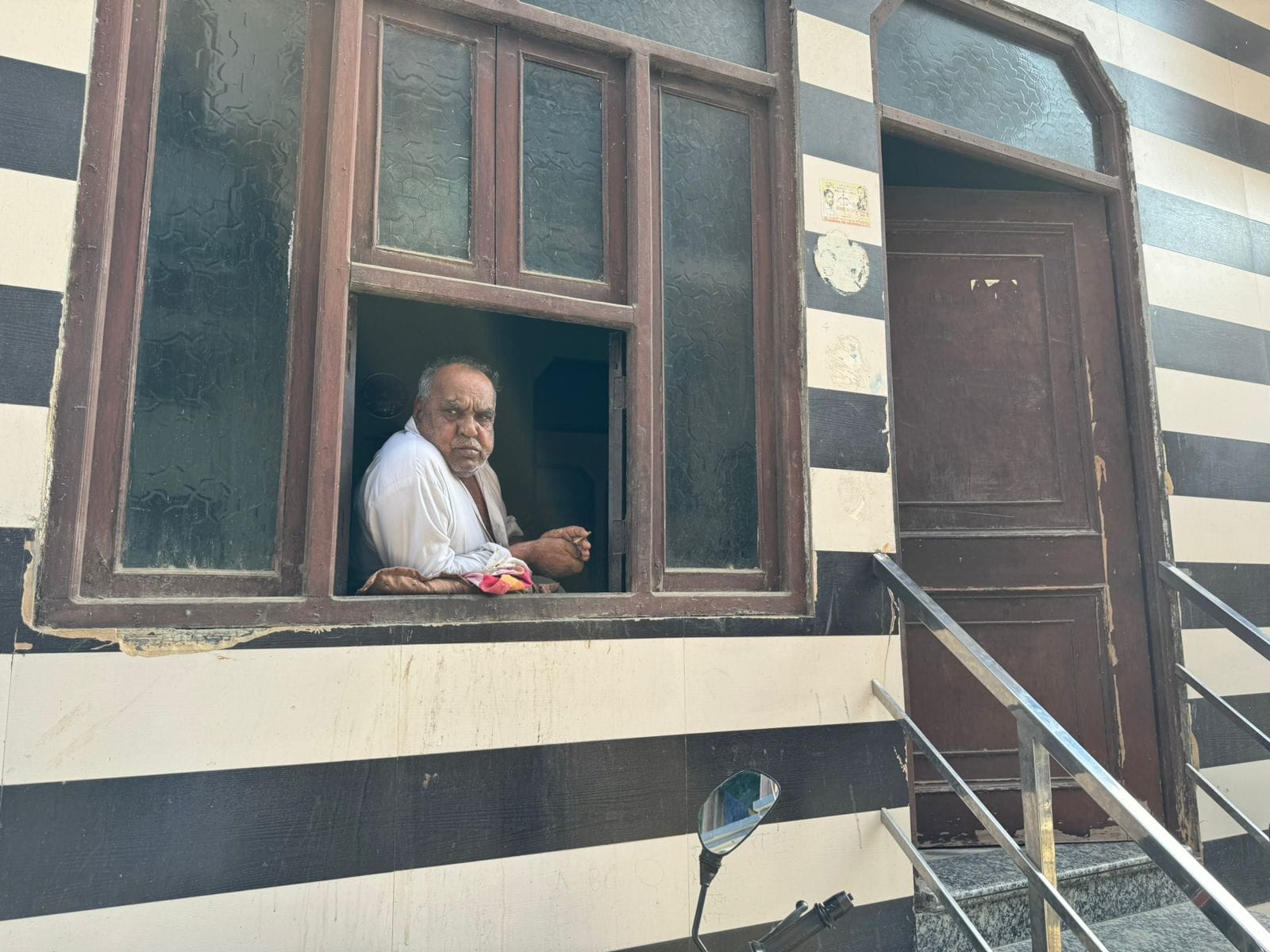 A neighbour peeping out of his window to watch the gathering of mourners in Nanak Colony of Kaithal
