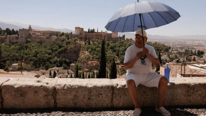 A tourist uses an umbrella at San Nicolas viewpoint in front of La Alhambra, during a hot summer day in Granada, Spain, July 22, 2024. REUTERS/Jon Nazca