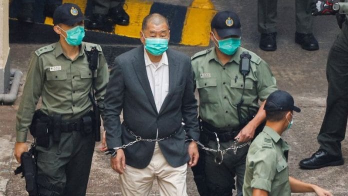 Jimmy Lai in handcuffs, surrounded by three guards