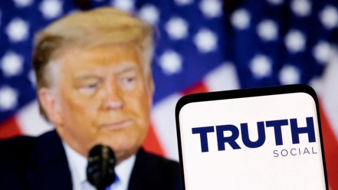 The Truth social network logo is seen on a smartphone in front of a display of former U.S. President Donald Trump in this picture illustration taken February 21, 2022 | Reuters