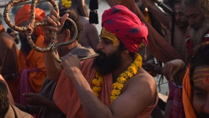 A young Naga saint at Sangam Bank blows on a ceremonial horn, ushering seekers