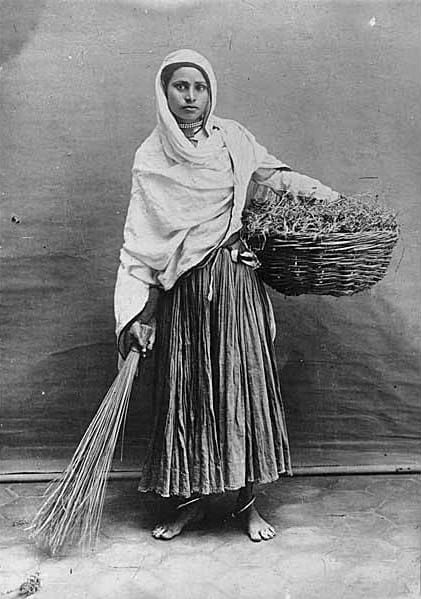 Studio portrait of a young woman with a basket and broom. India, c. 1921