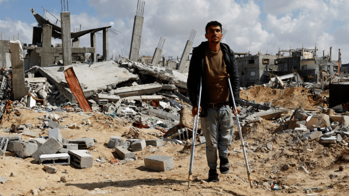 A Palestinian man walks with crutches amidst the rubble of buildings destroyed during the Israeli offensive, amid a ceasefire between Israel and Hamas, in Rafah in the southern Gaza Strip February 16, 2025 | Reuters