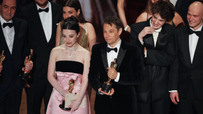 Director Sean Baker stands beside Best Actress winner Mikey Madison after 