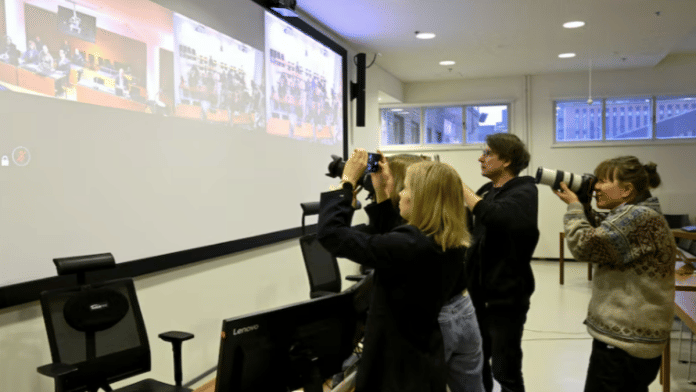 Members of the media gather near a screen as Yan Petrovsky, also known as Voislav Toden, an ex-commander of the Russian far-right extremist Rusich paramilitary group, who is suspected of committing war crimes in Ukraine, attends a trial, as projected on a screen, in Helsinki, Finland | Lehtikuva/Heikki Saukkomaa via Reuters